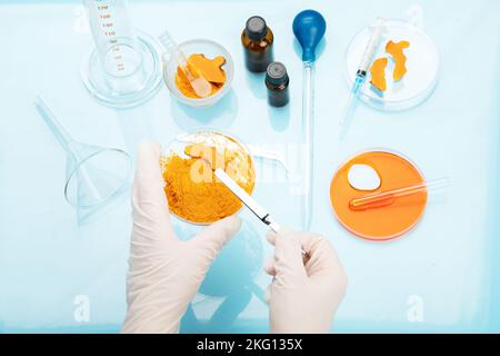 Ricerca medica delle proprietà curcuma con l'aiuto di attrezzature di laboratorio, donna in guanti di prova curcuma polvere. Vista dall'alto. Foto Stock