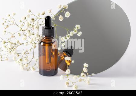 flacone di vetro con pipetta contro uno specchio rotondo e gypsofila. prodotto per la cura della pelle secco. siero per idratare la pelle. layout del marchio Foto Stock