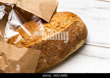 Pane fresco di grano saraceno su fondo di legno bianco. Una pagnotta di pane in un pacchetto. Foto Stock