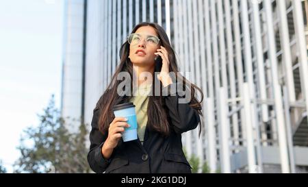 Donna di affari latina con gli occhiali che parlano sul telefono delle cellule in un'area di affari. Foto Stock