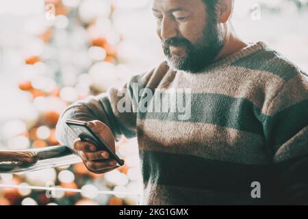 Un uomo che fa la chiamata telefonica all'interno di un centro commerciale nel mese di natale di dicembre con l'albero di festa decorato in backgorund. Concetto di nuovo anno x Foto Stock