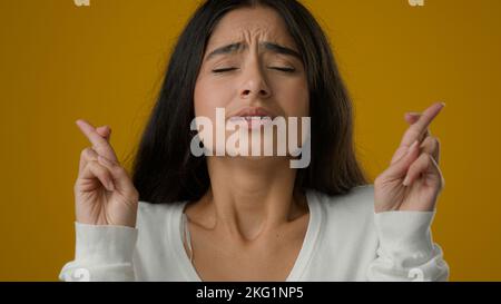 Primo piano ritratto in studio sfondo giallo indiano etnia donna ragazza donna femmina rende desiderio croci dita per buona fortuna attende desiderio di pregare Foto Stock