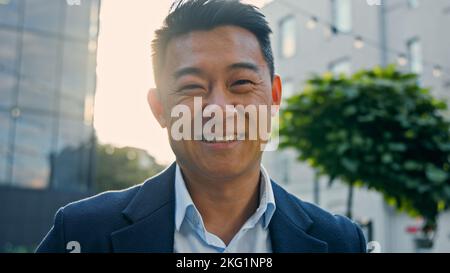 Uomo d'affari asiatico felice uomo d'affari di mezza età che ride sincero all'aperto in città emotivamente ridere sorriso con scherzo situazione divertente divertirsi Foto Stock