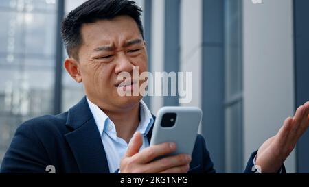 Primo piano asiatico di mezza età uomo adulto pazzo infelice uomo d'affari sentirsi infastidito con l'uso di smartphone rotto problema batteria scarica arrabbiato avere problema Foto Stock