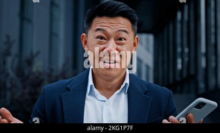 Felice scioccato stupito soddisfatto vincitore di successo asiatico 40s uomo di mezza età all'aperto vincere con il cellulare online scommessa business vittoria premio offerta Foto Stock