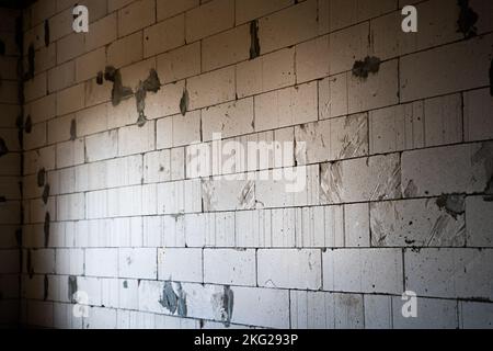 Una parete vuota di mattoni di cemento aerato bianco in una stanza scura di una casa incompiuta Foto Stock