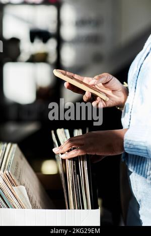 Primo piano di una giovane donna che gira tra i dischi vintage del negozio Thrift e che gira video su smartphone, illuminati dalla luce del sole Foto Stock