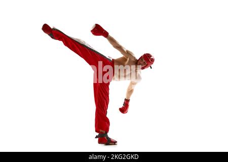 Calcio alla gamba. Giovane kickboxer professionista che indossa casco e guanti da boxe in movimento isolati su sfondo bianco. Sport, competizione, energia, combattimento Foto Stock