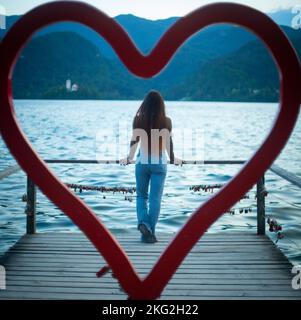 Una vista dalla decorazione a forma di cuore di una giovane femmina che gode di una vista sul mare su un molo di legno Foto Stock
