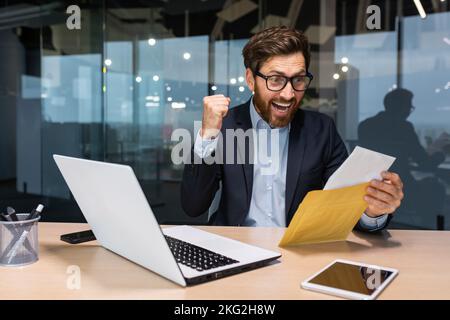 Investitore di successo imprenditore ha ricevuto una lettera di notifica dalla banca con buone notizie, l'imprenditore apre la busta legge e si rallegra della notizia, l'uomo è soddisfatto dei risultati . Foto Stock