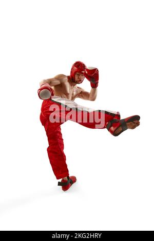 Giovane kickboxer professionista che indossa casco e guanti da boxe in movimento isolati su sfondo bianco. Sport, competizione, energia, sport di combattimento Foto Stock