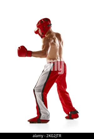 Gancio sinistro. Giovane kickboxer professionista che indossa casco e guanti da boxe in movimento isolati su sfondo bianco. Sport, competizione, energia, combattimento Foto Stock