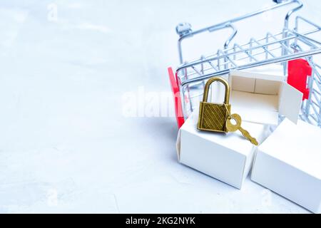 Carrello per la spesa in miniatura rovesciato con scatole di consegna e lucchetto con chiave. Shopping online e concetto di privacy. Foto Stock