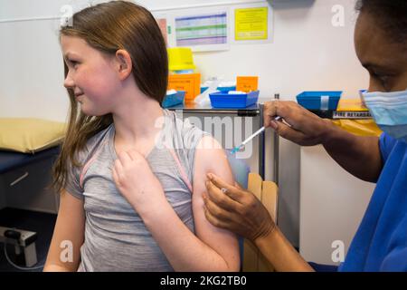 Una bambina di 10 anni riceve il vaccino mRNA COVID-19 Comirnarty 10 per vaccinarla contro l'infezione da Omicron Delta o da altre varianti esistenti di coronavirus. L'infermiere ritira l'ago dopo la somministrazione dell'iniezione presso il centro sanitario locale di Teddington. REGNO UNITO. (132). Il bambino che riceve il vaccino è modello rilasciato. Foto Stock