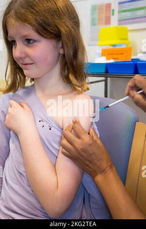 Una bambina di 8 anni riceve il vaccino mRNA COVID-19 Comirnarty 10 per vaccinarla contro l'infezione da Omicron Delta o da altre varianti esistenti di coronavirus. L'infermiere ritira l'ago dopo la somministrazione dell'iniezione presso il centro sanitario locale di Teddington. REGNO UNITO. (132). Il bambino che riceve il vaccino è modello rilasciato. Foto Stock