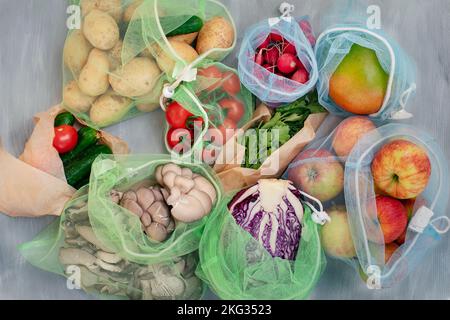 Alimenti per frutta e verdura in sacchetti a rete riutilizzabili su sfondo grigio in legno, vista dall'alto. Zero rifiuti e concetto di ecocompatibilità Foto Stock