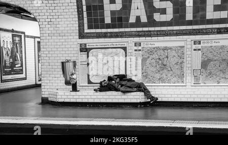 Un colpo in scala di grigi di un uomo senza casa che dorme in una stazione della metropolitana a Parigi, Francia. Foto Stock