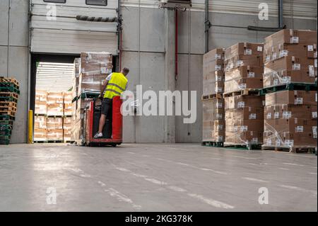 Ripresa di un carrello elevatore elettrico operatore maschio solleva pallet con scatole di cartone in un magazzino Foto Stock