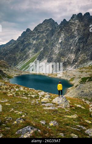 Donna escursionista Esplora il fantastico paesaggio e goditi la vista vicino a un lago di montagna in giacca gialla, High Tatra, Slovacchia Foto Stock