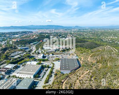 Scatto aereo stupefacente zona industriale circondata da varie infrastrutture, verde e molti veicoli parcheggiati in file nel Var, Francia Foto Stock