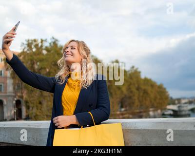 Donna Bionda sorridente che fa un selfie con i sacchetti di shopping in mano Foto Stock