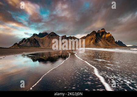 Luce del sole su Vestrahorn, penisola di Stokksnes. Golden hour shot con riflessione al crepuscolo e ripple della linea di testa sulla spiaggia di sabbia nera. Ghiaccio sud-orientale Foto Stock