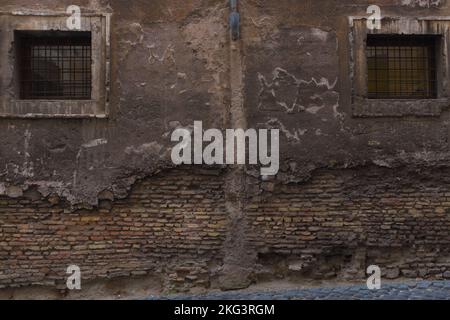 Vecchio muro di mattoni con due finestre quadrate con griglie. Cartolina da Trastevere a Roma. Vecchi strati attestano la storia della Città Eterna. Foto Stock