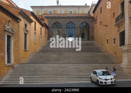 Uomo e donna si rilassano all'esterno di una piccola auto bianca parcheggiata ai piedi dei gradini di Palazzo nuovo. In Piazza del Campidoglio a Roma. Foto Stock