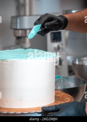cake designer levigare una torta bianca ghiacciata con crema di burro blu chiaro turchese con spatola Foto Stock