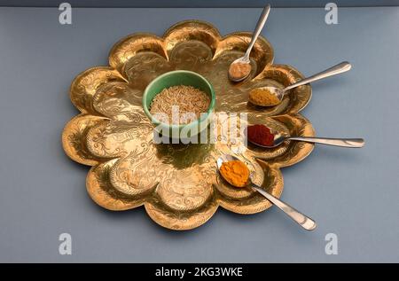 Il riso in una ciotola di ceramica verde sedette su un antico vassoio indiano circondato da cucchiaini da tè contenenti peperoncino, curcuma, zenzero e curry in polvere a base blu Foto Stock