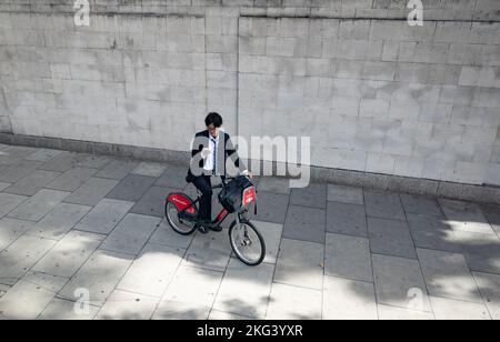Giovane dirigente asiatico su una bicicletta pubblica con il suo smartphone Foto Stock