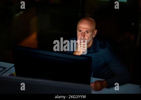 Foto di serio uomo d'affari premuroso seduto al tavolo con il computer in ufficio in tarda serata. Foto Stock