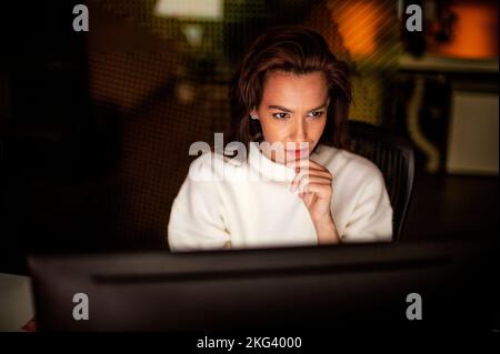 Ripresa di una donna d'affari seria e premurosa seduta al tavolo con un computer in ufficio a tarda sera. Foto Stock