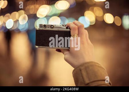 Ragazza hipster con fotocamera retrò che scatta foto della città notturna, punto di vista ripresa Foto Stock