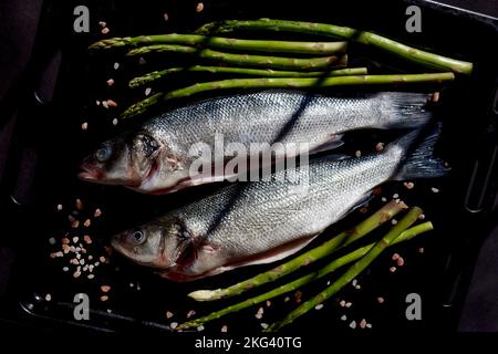 pesce di mare crudo, asparagi, sale su fondo nero Foto Stock