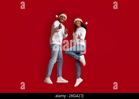 Allegro coppia nera che indica la macchina fotografica sul rosso, celebrando il Natale Foto Stock