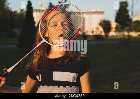 Ritratto di ragazza che guarda attraverso la racchetta badminton al parco Foto Stock