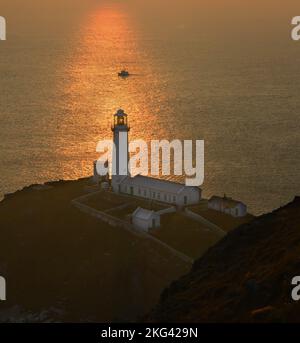Faro di South Stack, Anglsey, Galles del Nord, Regno Unito al tramonto in una calda serata. La luce del sole che illumina il faro e una barca di passaggio. Foto Stock