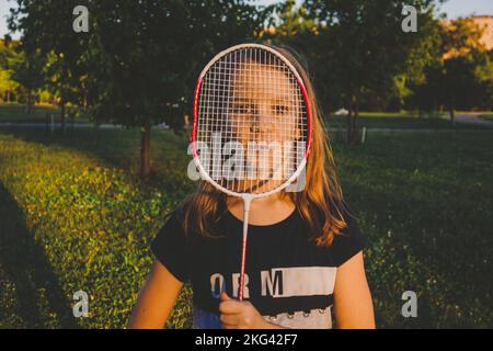 La ragazza sta guardando attraverso una racchetta badminton nel parco in una giornata estiva Foto Stock