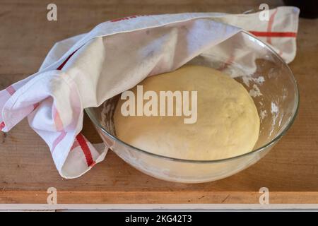 Pasta di lievito fatta in casa ricoperta di tovagliolo di cotone in un recipiente di vetro Foto Stock