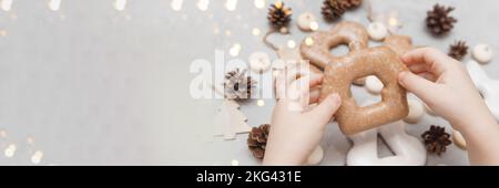 Le mani dei bambini tengono un pan di zenzero a forma di casa. Il concetto di dolci natalizi, giocattoli, ghirlande e bokeh. Arredamento per le vacanze di Capodanno. Foto Stock