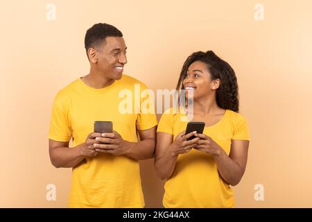 Sposi afro-americani felici che usano i cellulari, la rete o chattare con gli amici, guardandosi l'un l'altro Foto Stock