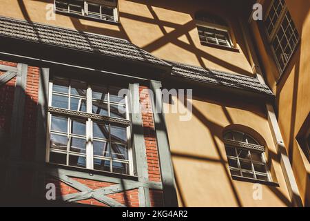 Edificio residenziale con pareti in mattoni gialli e rossi e finestre in legno. Ombre nere cadono sulla parete dell'edificio dal sole della sera d'autunno. Foto Stock