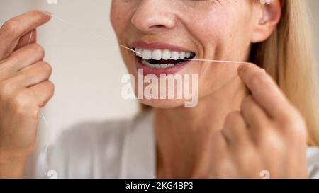 Concetto di cura dei piedi e di trattamento orale. Primo piano vista ritagliata di una donna di mezza età irriconoscibile utilizzando filo interdentale Foto Stock