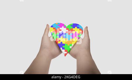 Il simbolo dell'autismo è un puzzle multicolore sotto forma di cuore nelle mani di genitori premurosi. Cura e amore per i bambini disor spettro autismo Foto Stock