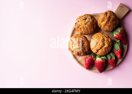 Muffin alle fragole su una tavola di legno su sfondo rosa. Spazio di copia. Foto Stock