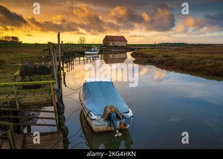 Barche e fienile di carbone sull'estuario a Thornham Old Harbour al tramonto, Thornham, Norfolk, Inghilterra Foto Stock