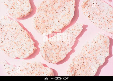 Molte macchie di scrub su sfondo rosa. Consistenza del corpo o del viso scrub - macchie di albicocca e semi di pesca. Prodotto naturale per la cura della pelle per esfoliazione Foto Stock