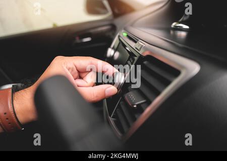 La mano del conducente regola il volume sul cruscotto dell'autoradio. Foto Stock