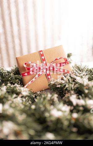 Scatola regalo in cartone Kraft legata con corda di iuta ruvida su fondo di legno grigio con rami di albero di Natale e decorazioni natalizie Foto Stock